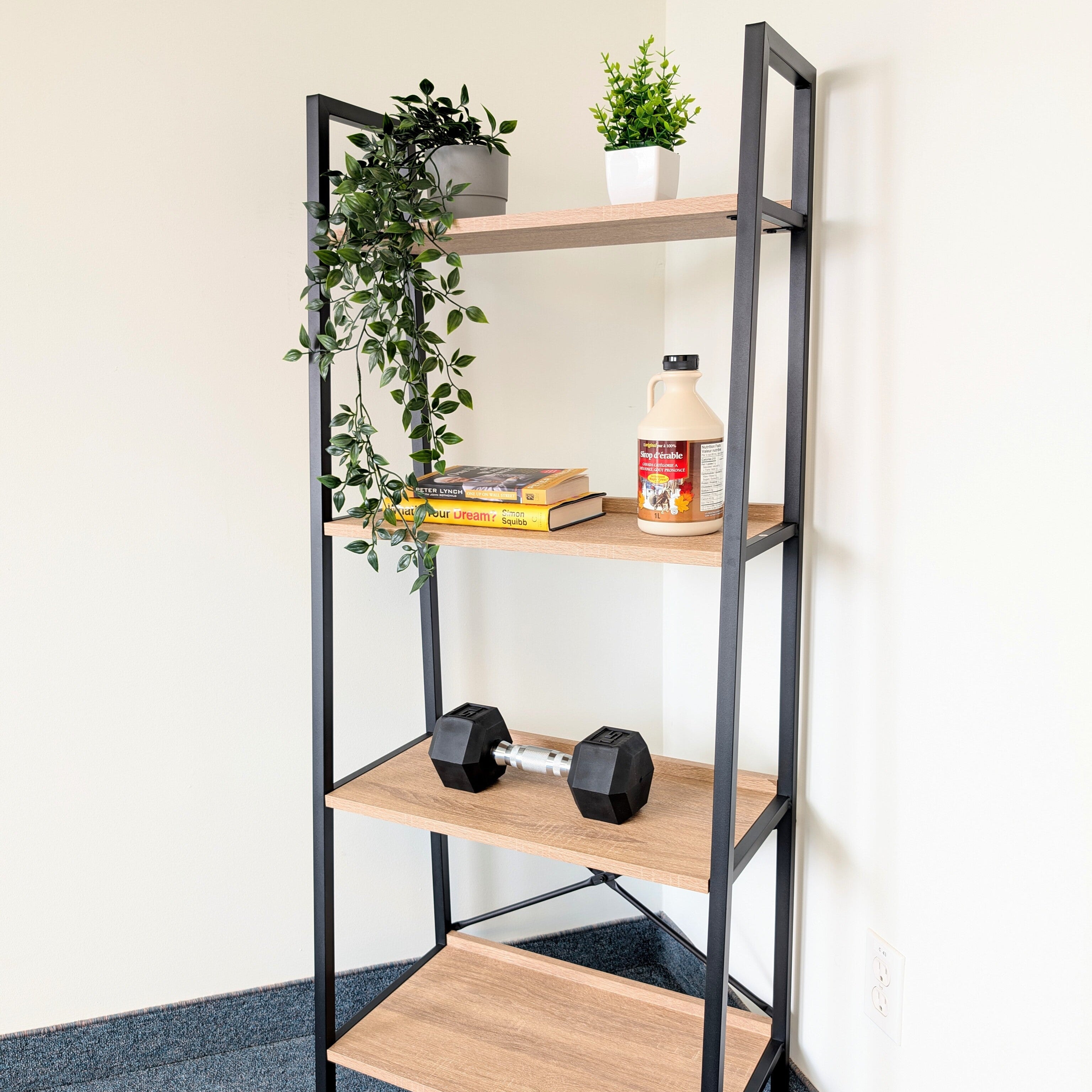 Bookshelf with wooden shelves and black metal frame, holding books, a bottle, and dumbbells.
