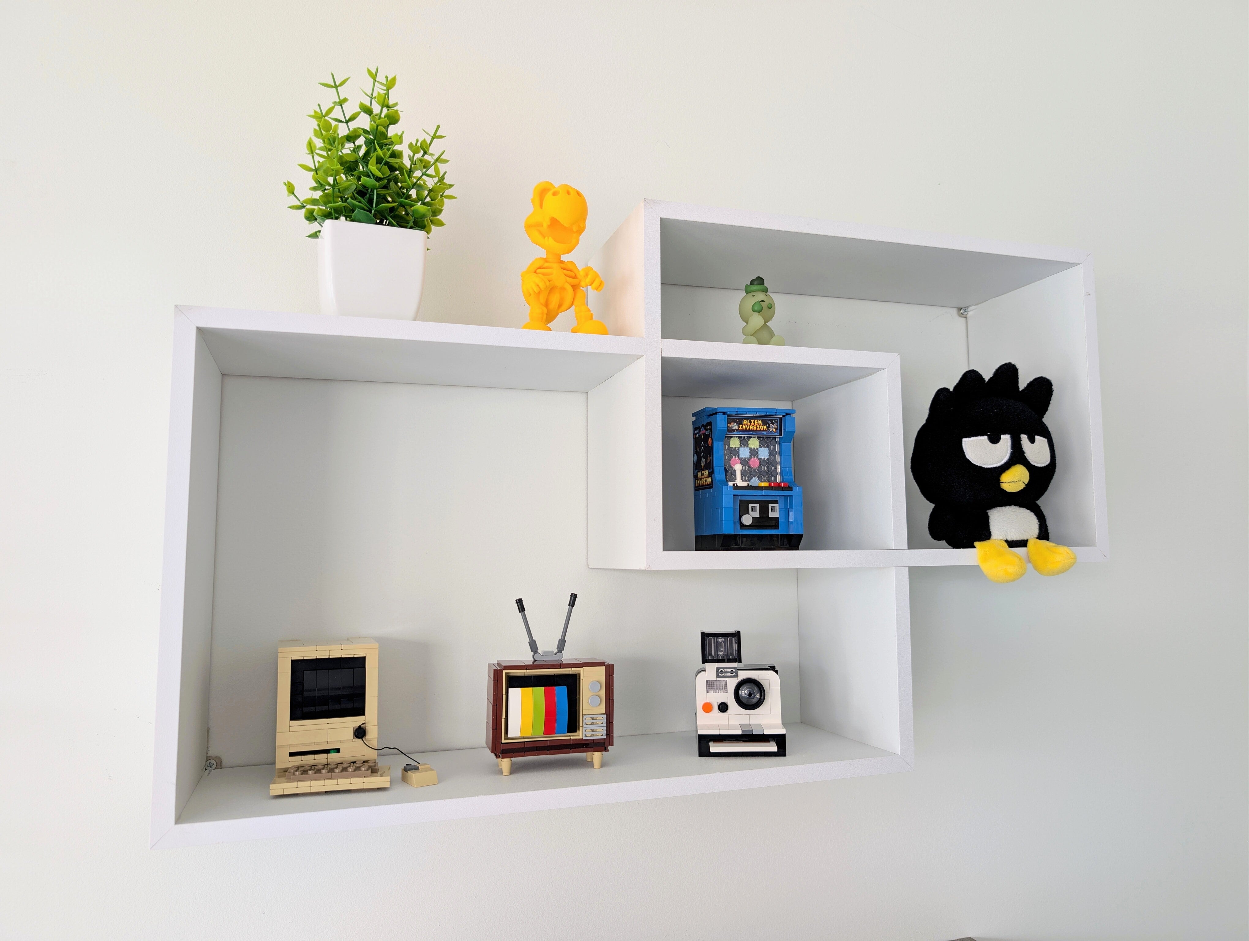 White wall shelves with decorative items including a plant, toys, and vintage-style electronic devices.