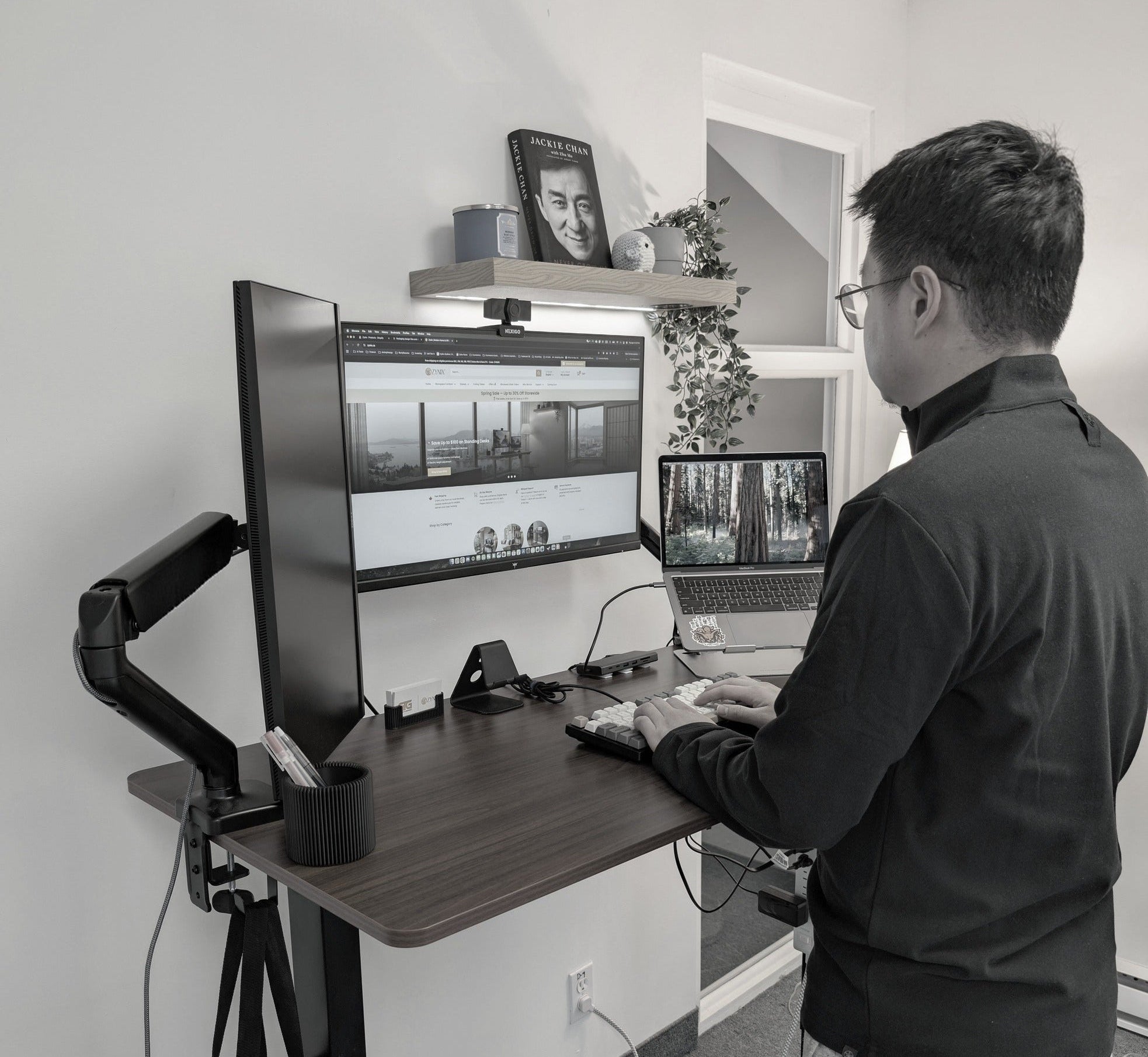 Person using a standing desk with multiple computer monitors in a home office setting.