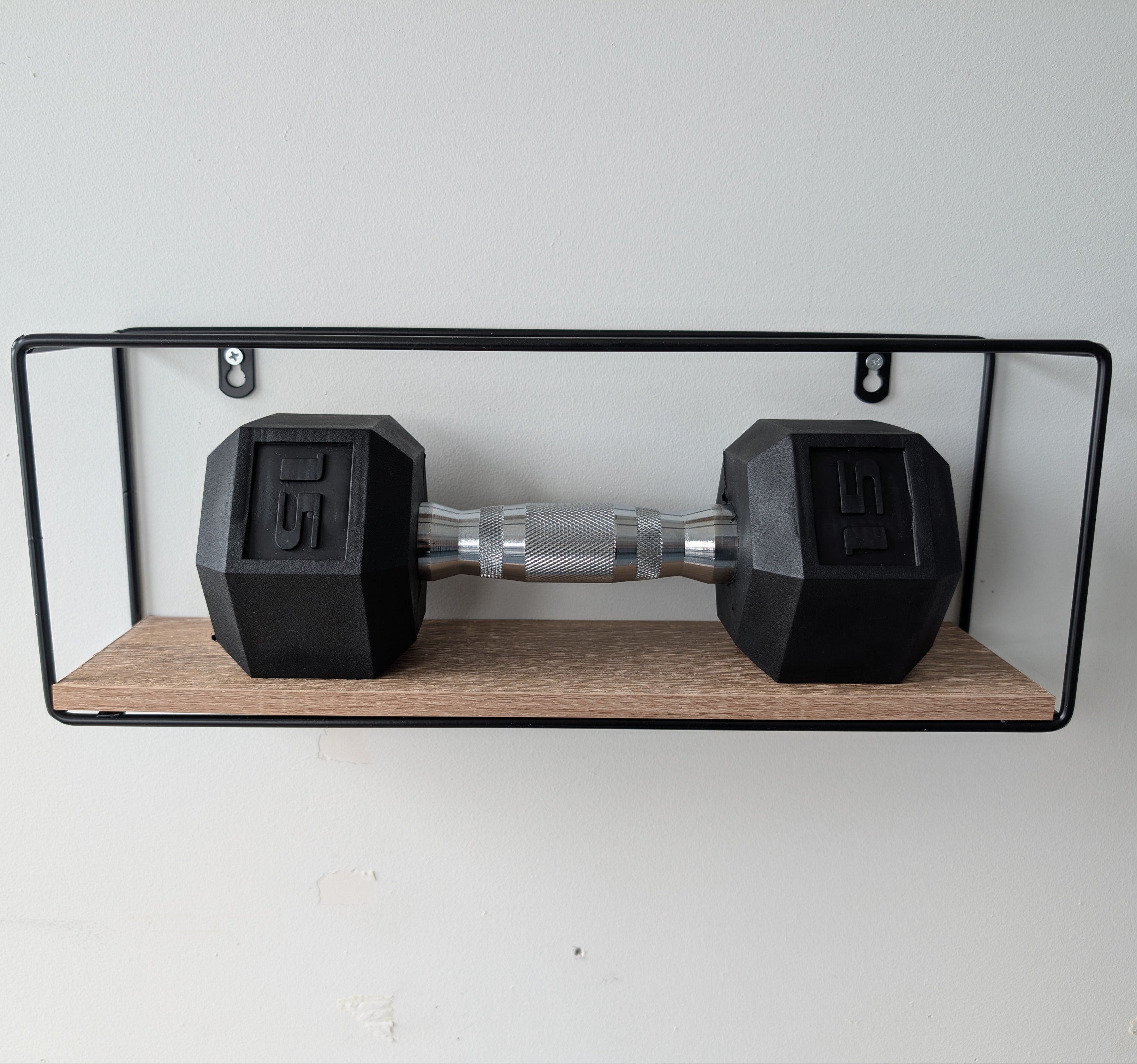 Pair of black dumbbells on a wooden shelf against a white wall