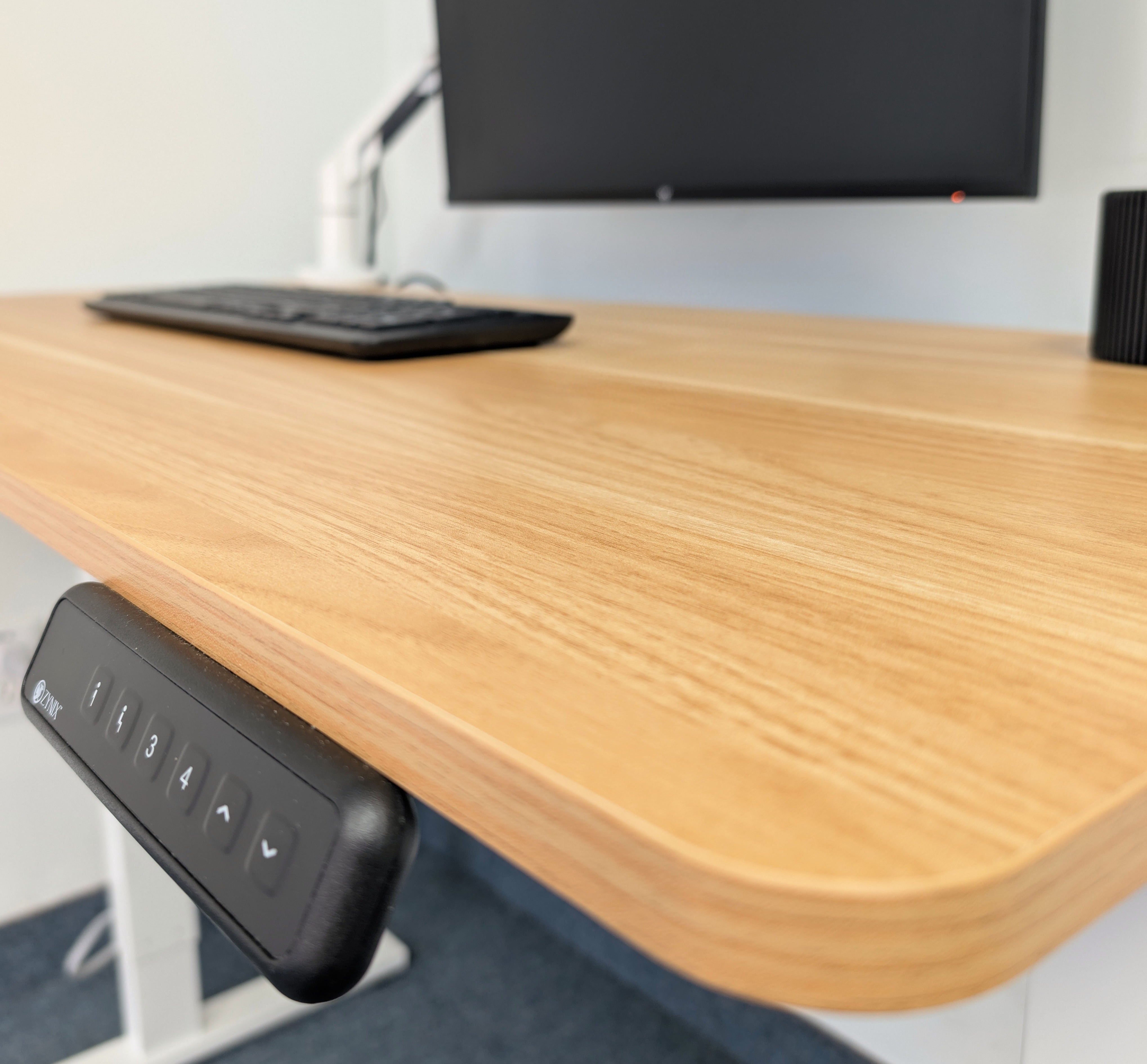 Wooden desk with a computer monitor, keyboard, and control panel.
