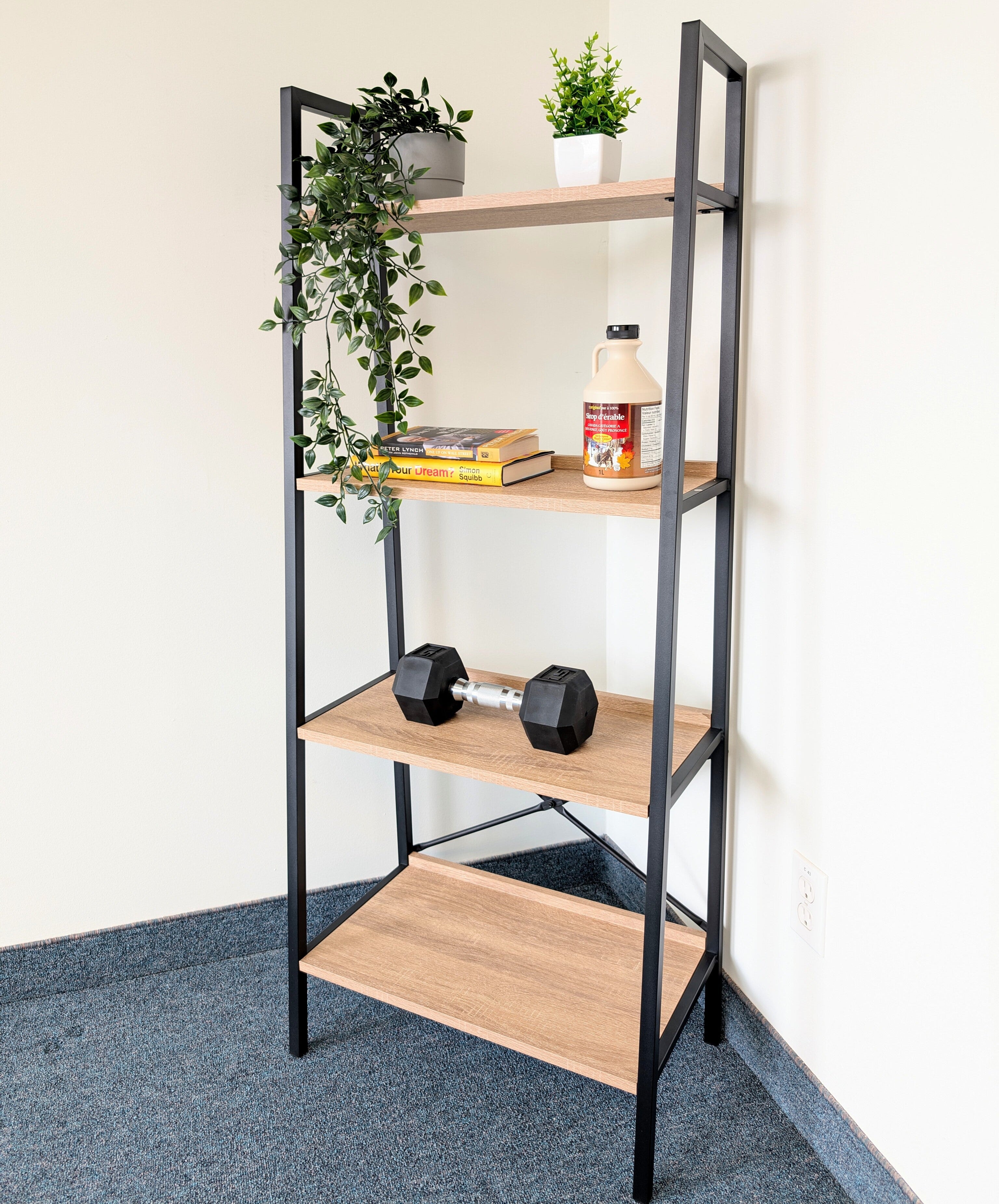 Bookshelf with wooden shelves and black metal frame, holding books, a bottle, and dumbbells.