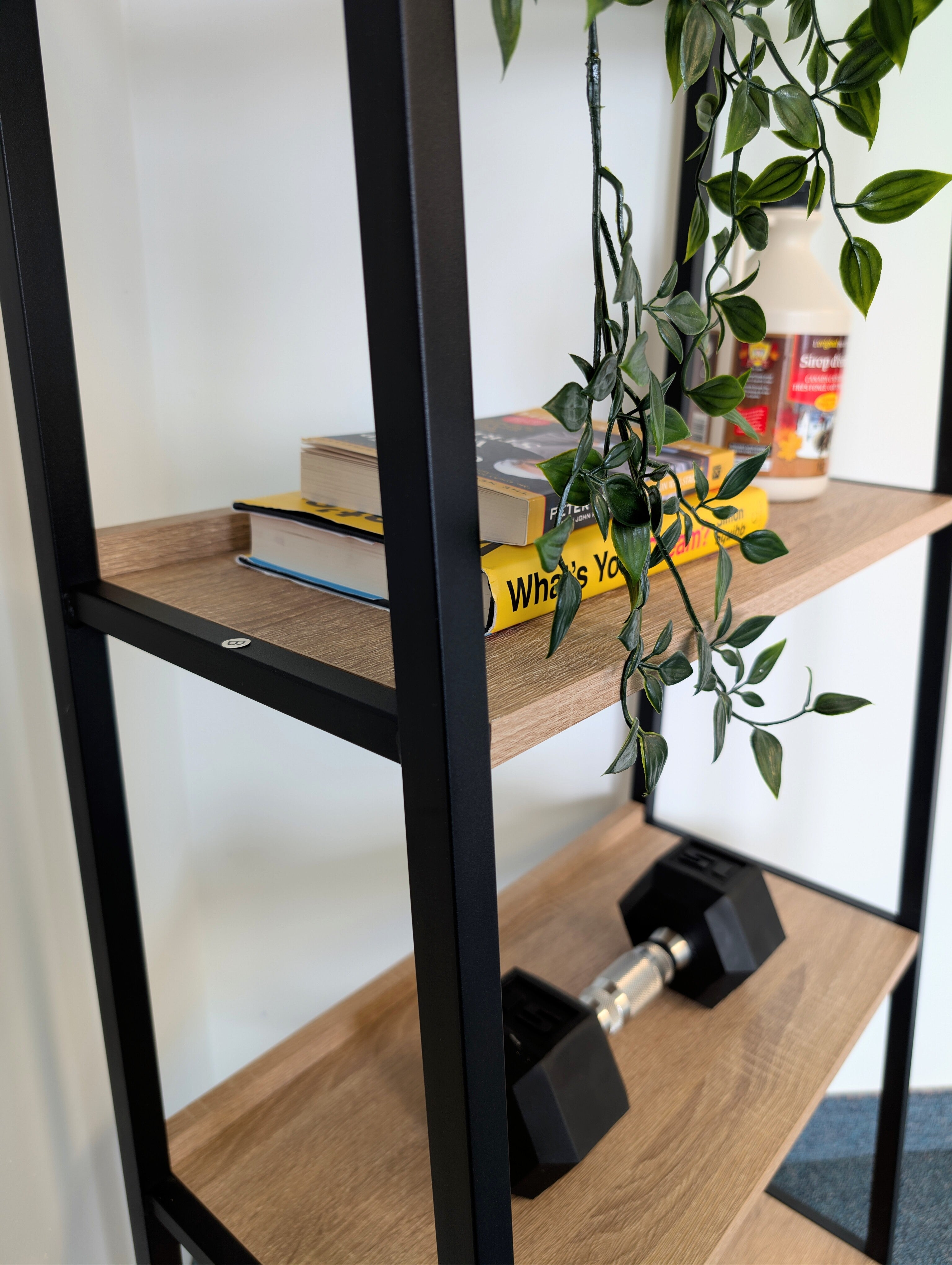 Bookshelf with wooden shelves and black metal frame, holding books and a dumbbell.