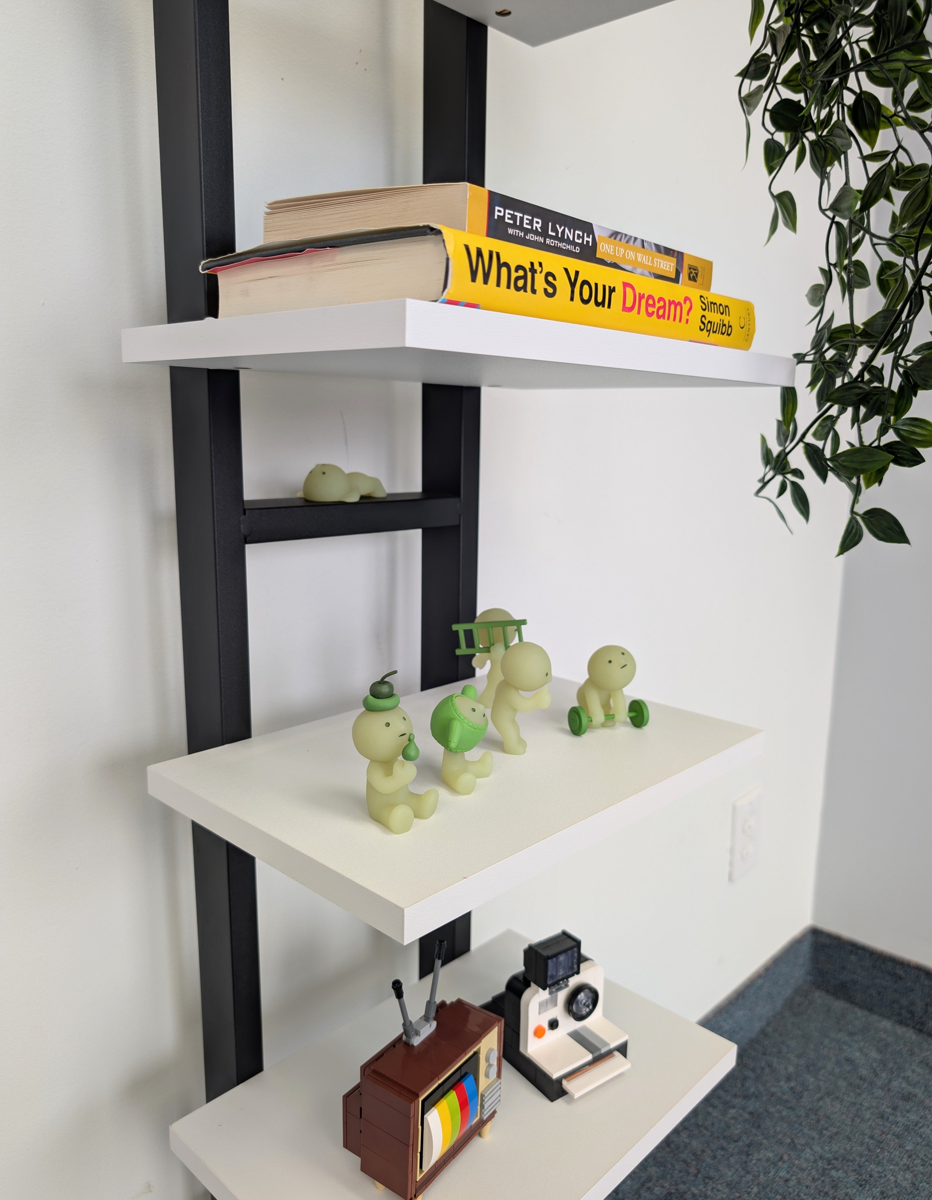 Corner shelf with books, small figurines, and a camera on white and black shelves.