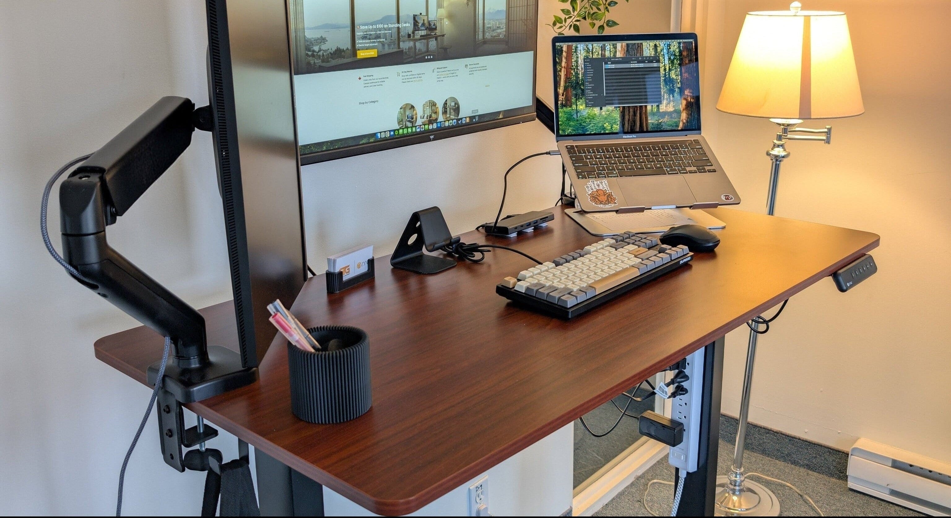 Home office setup with a standing desk, computer monitors, and a lamp.