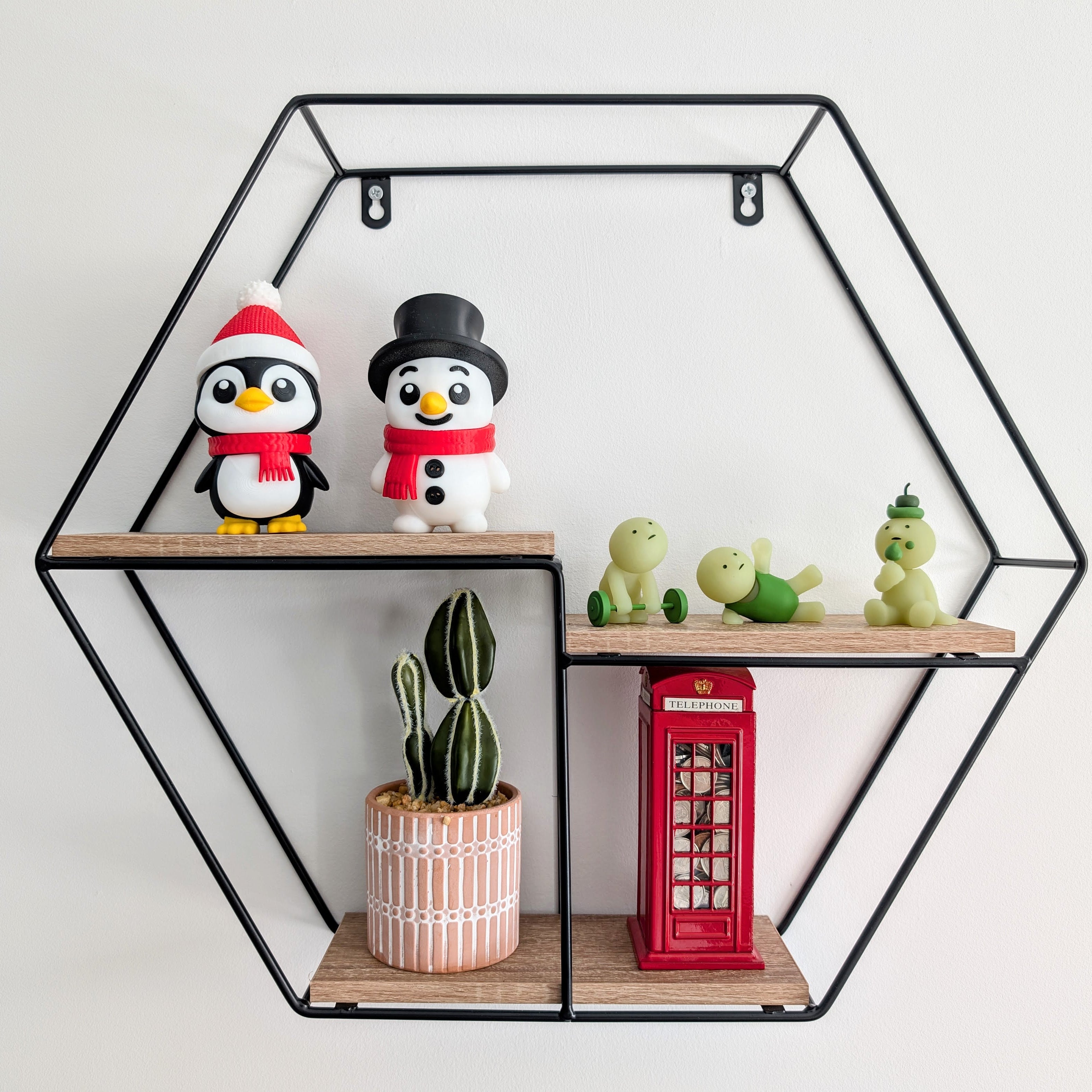 Hexagonal wall shelf with decorative items including penguins, a potted plant, and a red telephone box.